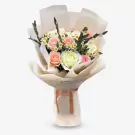Bouquet of pink and white roses with small white daisies and greenery, wrapped in light-colored paper with a ribbon.