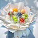A fruit bouquet with clear spheres of grapes, strawberries, blueberries, apples, and oranges, surrounded by baby's breath.