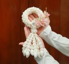 Hands holding a white floral garland with pink accents and a beaded center.