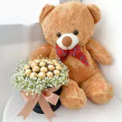 Teddy bear with a box of Ferrero Rocher chocolates and white flowers.