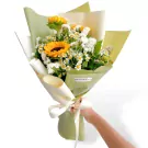 Bouquet of sunflowers and white dry statice flowers, wrapped in green and cream paper with a ribbon.