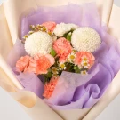 Bouquet of white chrysanthemum, pink carnations and small white daisies, wrapped in lavender and cream paper.