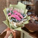 Pink carnations and dusty miller bouquet wrapped in green paper, tied with a ribbon.