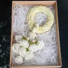 White fresh malai with jasmine and roses in a box lined with white paper shred.