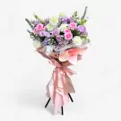 A tall floral stand with pink, purple, and white flowers, wrapped in pastel pink and peach paper.