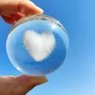 Crystal ball with heart-shaped cloud on a finger against a blue sky.