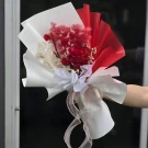 A bouquet of red dried flowers with white limonium, wrapped in white and red paper with a ribbon.
