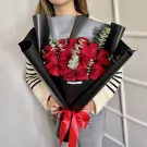 Woman holding a bouquet of 18 red roses wrapped in black paper and tied with a red ribbon.