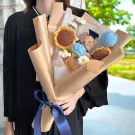 Crochet graduation bouquet with teddy bear, sunflowers, and daisies, tied with a blue ribbon.