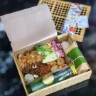 Khao Chae set in a wooden box with rice, mangoes, shrimp balls, fried toppings, and jasmine water.