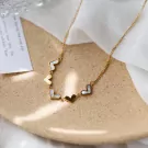Gold chain necklace with five heart-shaped charms, alternating between gold and white shell inlay.
