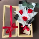 Wooden box with a bouquet of red roses and eucalyptus, tied with red ribbons.