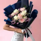 Bouquet of white and pink roses and dried flowers wrapped in dark blue paper with a white ribbon.
