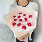 Woman holding a large bouquet of red, pink, and white satin roses with diamond centers, wrapped in pale peach paper.