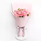 Pink gerberas and carnations in a pink bouquet with a grey ribbon on a white stand.