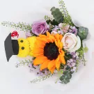 A graduation bouquet with a sunflower, roses, and a teddy bear wearing a grad cap.