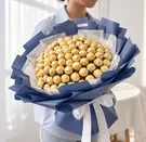 A person holds a large bouquet made of 100 Ferrero Rocher chocolates wrapped in navy blue and white paper.