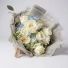 A bouquet of white roses and blue hydrangeas with daisy accents, wrapped in patterned paper with a "Thank You" tag.