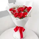 A bouquet of 15 deep red roses with baby's breath, wrapped in white paper and tied with a red ribbon.