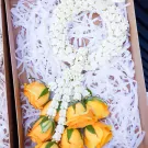 Yellow roses and a white flower garland in a box with white shred filler.