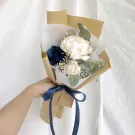 A bouquet of white and blue roses, peonies, and baby's breath, wrapped in brown paper and tied with a blue ribbon.