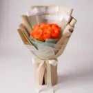 Bouquet of vibrant orange roses wrapped in brown paper with a cream ribbon bow.