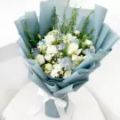 A light blue bouquet of white carnations, roses, lisianthus, and gypsophila tied with a white ribbon.