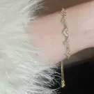 Gold chain bracelet with five alternating sparkly and white heart charms on a wrist.