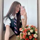 A girl in a school uniform takes a mirror selfie with a bouquet of orange and white carnations.