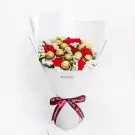 Bouquet of red carnations, white statice, and Ferrero Rocher chocolates wrapped in white paper with a burgundy ribbon.