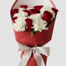 Bouquet of red roses and white carnations in red paper, tied with a white ribbon.