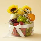 A fruit box with strawberries, grapes, cherries, an orange, and sunflowers, tied with a white ribbon.