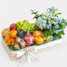 Fruit box with grapes, oranges, dragon fruit, kiwi, and blue flowers, wrapped in plastic.