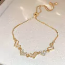 Gold chain bracelet with five heart charms, some inlaid with white material and others with small stones.