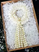 White flower garland with a tassel, adorned with a gold and pearl accent, in a gift box.