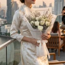 Woman in a traditional Chinese dress holds a bouquet of white roses on a city balcony.