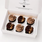 Six chocolate cupcakes in a white box, three chocolate and three milk chocolate, decorated with gold flakes and sprinkles.