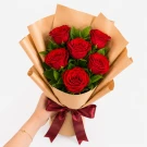 Woman holding a bouquet of six red roses wrapped in brown paper with a red ribbon.