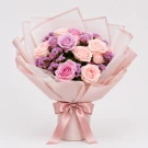 Pastel pink and purple rose bouquet wrapped in delicate pink paper with a ribbon.