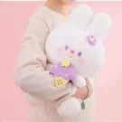 A white plush rabbit with purple flower and ice cream accessory, held by a person in a cream sweater.
