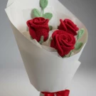 Crocheted red rose bouquet wrapped in white paper, tied with a red ribbon.