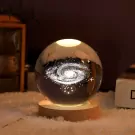 Crystal ball with Milky Way galaxy and stars illuminated from below, on a wooden base.