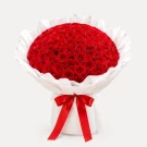 A large bouquet of 99 vibrant red roses, wrapped in white paper and tied with a red ribbon.