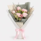 Pink roses, carnations, daisies, and caspia in a bouquet wrapped with white and cream paper, tied with a pink ribbon.