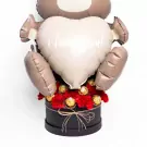 Teddy bear balloon holding heart with "i love you!", surrounded by red carnations and Ferrero Rocher chocolates in a black box.