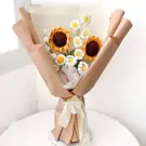 Crocheted sunflowers and white daisies in a tan paper bouquet tied with a cream ribbon.