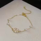 Gold bracelet with a white floral charm and pearls.