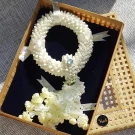 Artificial jasmine garland with pearls and blue gem in a woven basket.