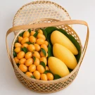 Woven bamboo basket filled with yellow Marian plums and mangoes on green leaves.