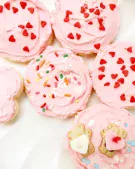 Pink frosted sugar cookies with heart and sprinkle decorations.